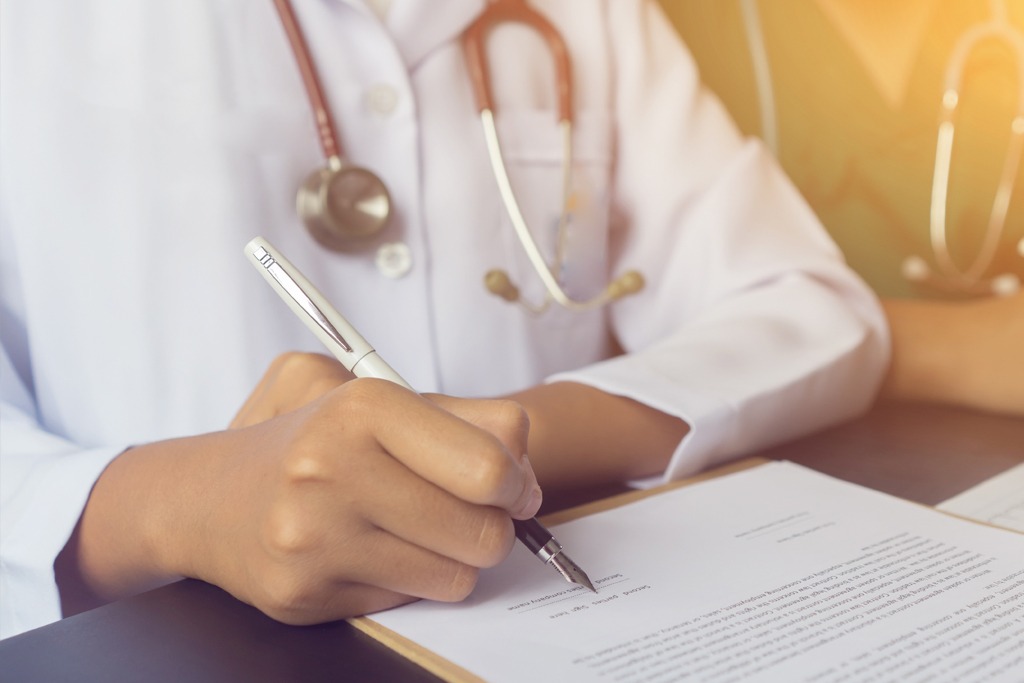 Physician doctor writing on medical health care record, patients discharge, or prescription form paperwork in hospital clinic discussing success medical healthcare, Medicine doctor's working concept 