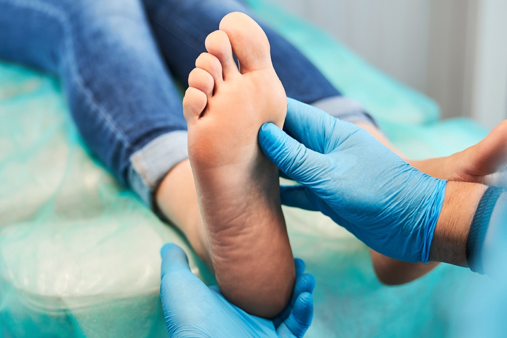 Unrecognized chiropodist on blue gloves examining toes and feet of female patient in medical center