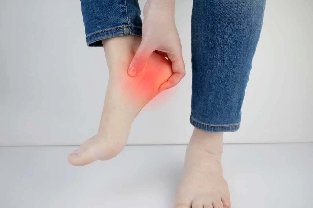 Woman suffering from heel pain. Inflammation or sprain of the tendon in the foot, heel spur, bursitis. The concept of diseases and pains in the leg